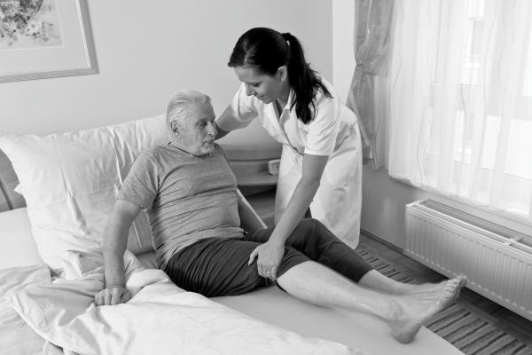 Auxiliar de saúde ajudando idoso a se posicionar em seu colchão para acamado