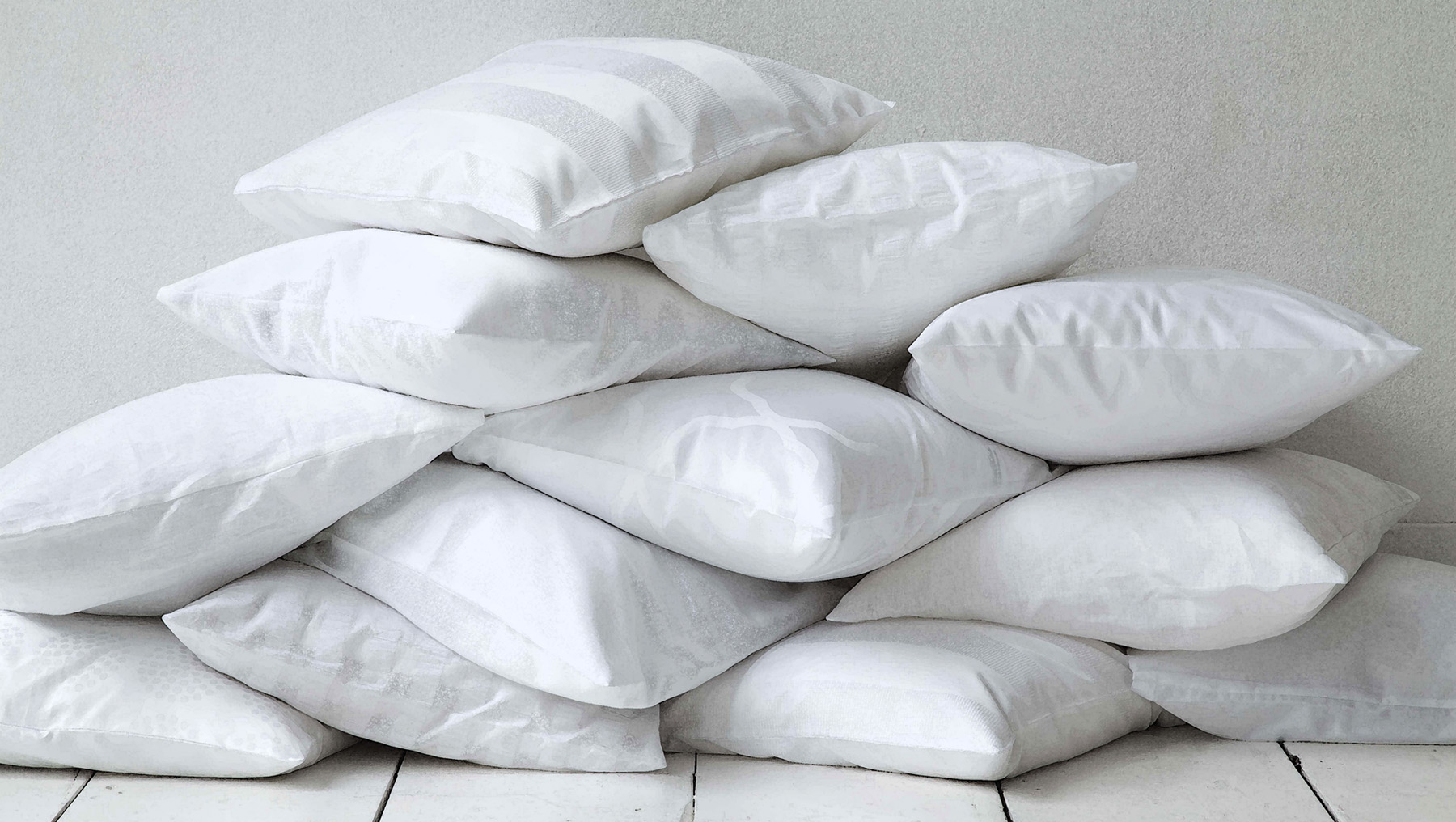 Pilha de travesseiros brancos sobre o chão, encostados em uma parede