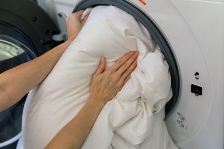 Mulher colocando um pillow top em uma máquina de lavar.