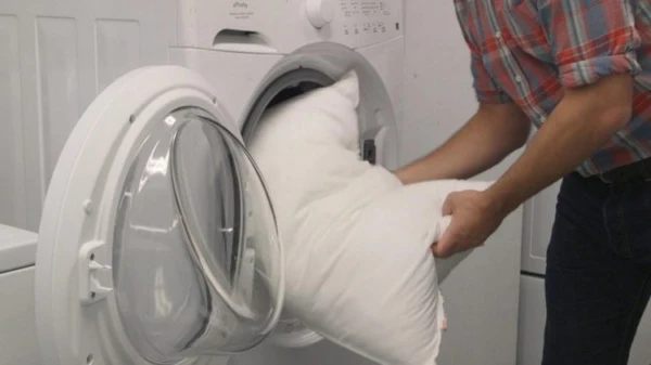 Homem colocando travesseiro de penas de ganso dentro da máquina de lavar.