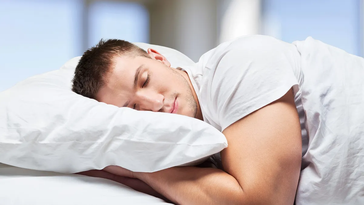 Homem jovem dormindo em um travesseiro de penas de ganso.