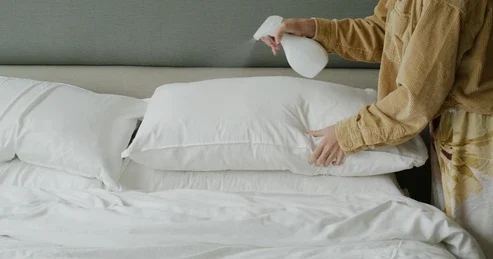 Mulher borrifando água de lençol sobre travesseiros.