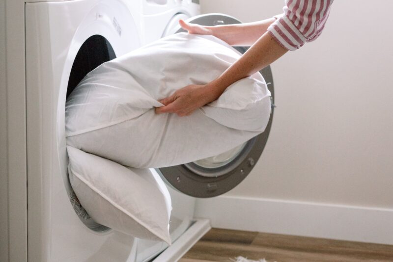 Mulher lavando travesseiro dentro da máquina de lavar.